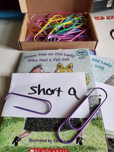 there is a box that has some paper clips in it and an open book on the table