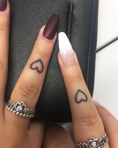 two fingers with hearts tattooed on them, one has a ring and the other has a heart