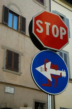 two street signs on top of each other in front of a building with shuttered windows