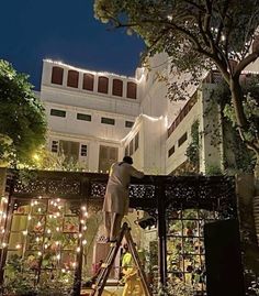 a man on a ladder in front of a building with christmas lights hanging from it