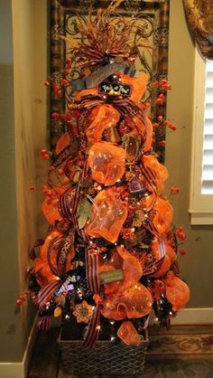 a decorated christmas tree in the corner of a room with an orange ribbon on it