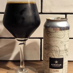 a can of beer next to a tall glass on a wooden table with white tiles