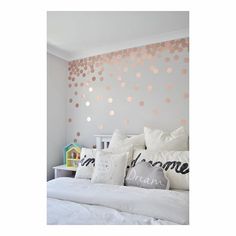 a white bed topped with lots of pillows next to a wall covered in pink and gold circles