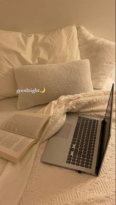 a laptop computer sitting on top of a bed next to an open book and pillow