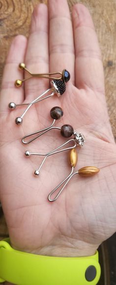 a person's hand holding five pins with different shapes and sizes on them in front of a wooden table