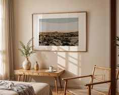 a bedroom scene with focus on the bed and desk in the foreground, there is a framed photograph hanging above the bed