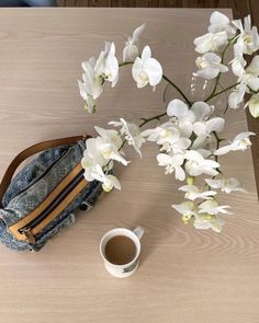 white flowers and a denim purse on a wooden table next to a cup of coffee