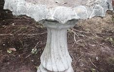 an old bird bath sitting in the middle of some grass and dirt on the ground