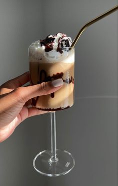 a hand holding a spoon over a drink in a glass with whipped cream and chocolate