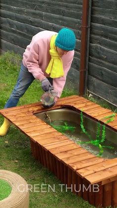 a man in pink jacket pouring water into a wooden table with plants growing out of it