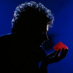 a man holding a red origami piece in his right hand and looking at it