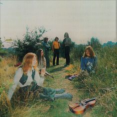 a group of people sitting on top of a grass covered field next to each other