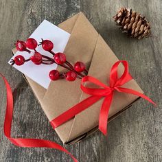 a brown box with red ribbon and some berries on it next to a pine cone