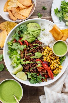 a white bowl filled with mexican food next to bowls of guacamole and tortilla chips