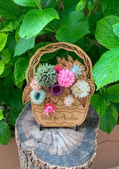 a wooden basket with flowers in it sitting on top of a tree stump next to green leaves