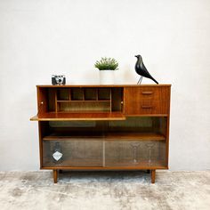 a wooden cabinet with a bird on top and two wine glasses sitting on the shelf