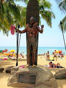 a statue of a man holding a surfboard on the beach