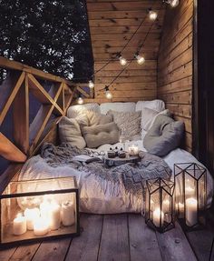 an outdoor bed with candles on it and lights strung from the ceiling over it, in front of a wooden wall