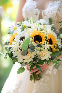 a bride holding a bouquet of sunflowers and greenery