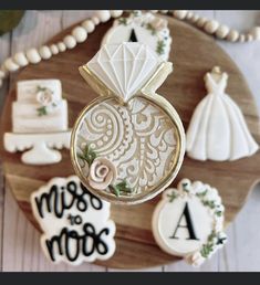 decorated cookies are arranged on a wooden platter with wedding rings and bride's dresses