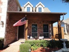 an american flag is on the front porch of a brick house with landscaping and shrubs