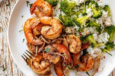 a white plate topped with shrimp, broccoli and rice next to a fork