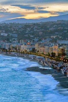 the beach is lined with people and buildings near the water's edge at dusk