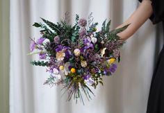 a woman holding a bouquet of flowers in front of a white curtain with purple and yellow colors