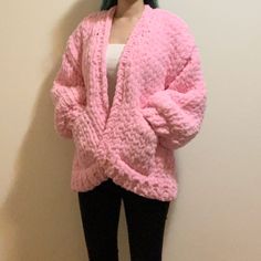 a woman standing in front of a wall wearing a pink sweater