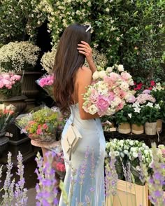 a woman in a blue dress is looking at flowers and holding her hands behind her head