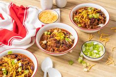 three bowls of chili and cheese on a wooden table