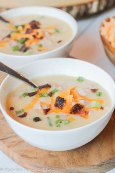 two white bowls filled with soup on top of a wooden cutting board next to bread