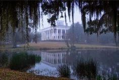 a large white house sitting on top of a lush green field next to a lake