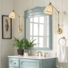 a bathroom with blue cabinets and two lights on the side of the vanity, along with a potted plant