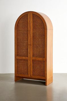 a wooden cabinet sitting on top of a cement floor next to a white wall with an arched door