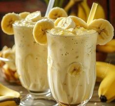 two glasses filled with banana milkshakes on top of a table next to bananas