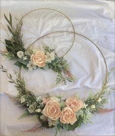 two circular wreaths with flowers and greenery on top of a white bed sheet