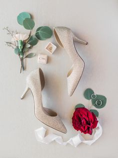 wedding shoes and boutonnieres laid out on a white surface with red flower