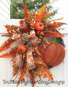 a wreath with pumpkins and leaves hanging on the side of a white fence in front of a house