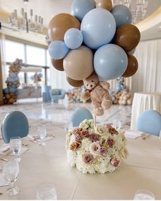 a teddy bear on top of a bunch of balloons in a room with tables and chairs