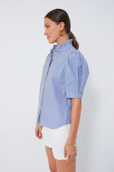 The Alicia Blouse is defined by it's puff sleeves, ruffled stand collar, and always on-trend blue and white stripes. Cut in the perfect length that looks great tucked in or left out, this effortlessly polished piece is great for year round wear thanks to its versatile styling options. Pair this feminine number with white denim during the warmer months and opt for trousers and a sweater layered on top for the cooler ones. Ruffle stand collar Puff sleeves Button front placket Tortoise shell button Spring Pinstripe Blouse With Striped Collar, Blue Blouse With Striped Collar In Relaxed Fit, Blue Blouse With Striped Collar And Short Sleeves, Striped Blouse With Puff Sleeves, Blue Relaxed Fit Top With Striped Cuffs, Blue Cotton Top With Striped Sleeves, Blue Cotton Top With Striped Collar, Blue Oversized Top With Striped Collar, Sweater Layering