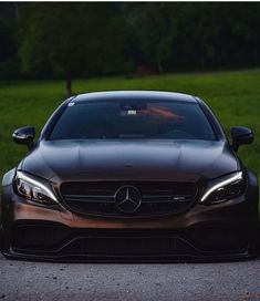 the front end of a black mercedes benz coupe parked on a road with grass and trees in the background