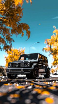 a black jeep parked on the side of a road in front of trees with yellow leaves