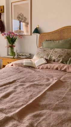 a bed with a pink comforter and two vases filled with flowers next to it