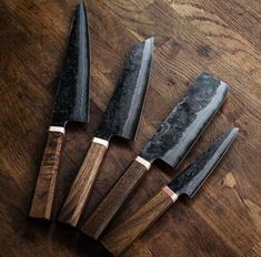 five knives sitting on top of a wooden table next to each other with black handles