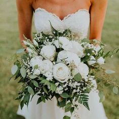 a bride holding a bouquet of white flowers and greenery on her wedding day in the grass