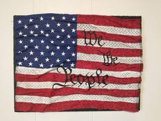 an american flag with we the people written on it, hanging on a white wall