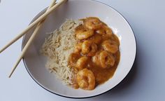 a bowl filled with rice and shrimp next to chopsticks on a white table