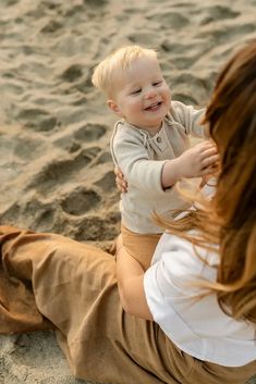 a woman holding a baby on the beach with her arm around it's head