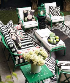 an outdoor living room with black and white furniture, green accents and flowers on the coffee table